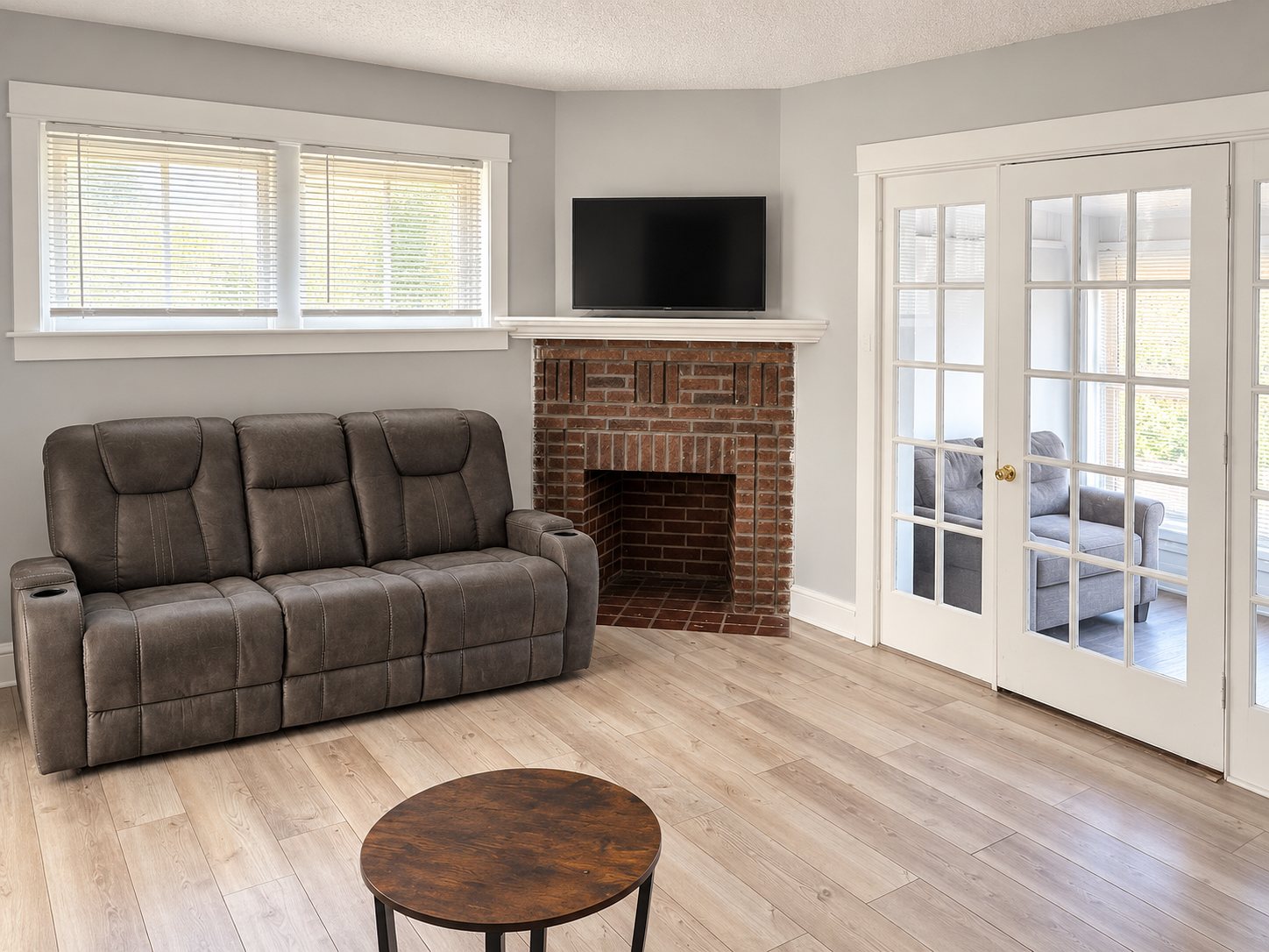 The living room of an Evo Living home: a sofa by a red brick fireplace, wood floors, and French doors opening to a second sitting room.
